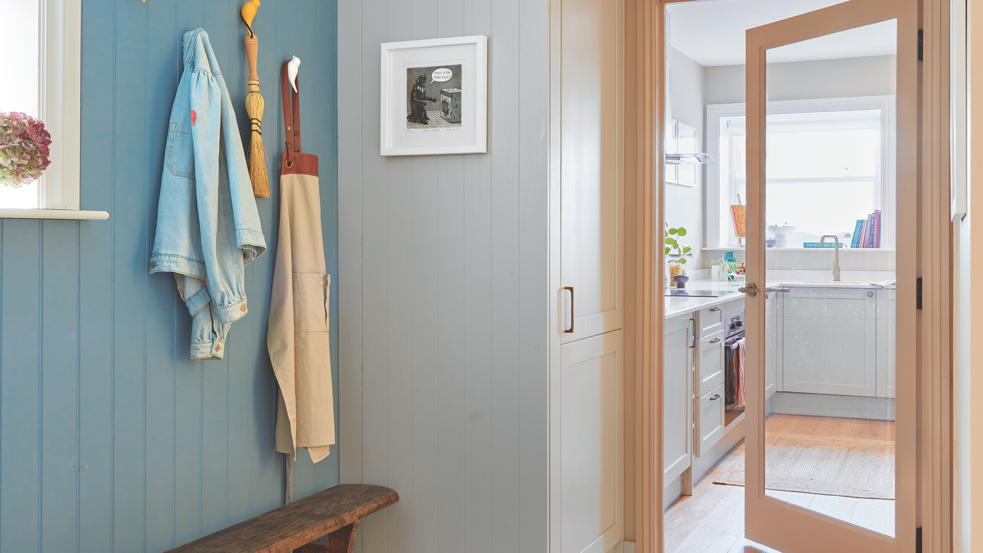 Blue hallway with patterned tiled floor, bench and storage hooks leading into a small kitchen.