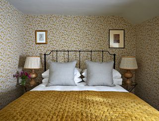 bedroom with wrought iron bed, yellow throw and yellow patterned wallpaper
