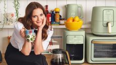 Drew Barrymore holding a coffee mug next to a stack of green small kitchen appliances