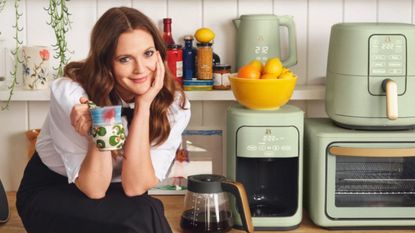 Drew Barrymore holding a coffee mug next to a stack of green small kitchen appliances