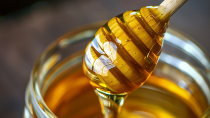 Honey being drizzled from a wooden dipper.