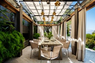 An outdoor pergola over a dining table with curtains around it