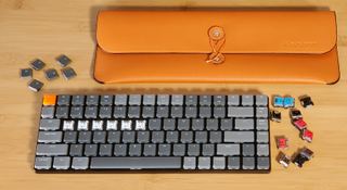 gray compact keyboard with extra keys and orange carrying case against light wood background
