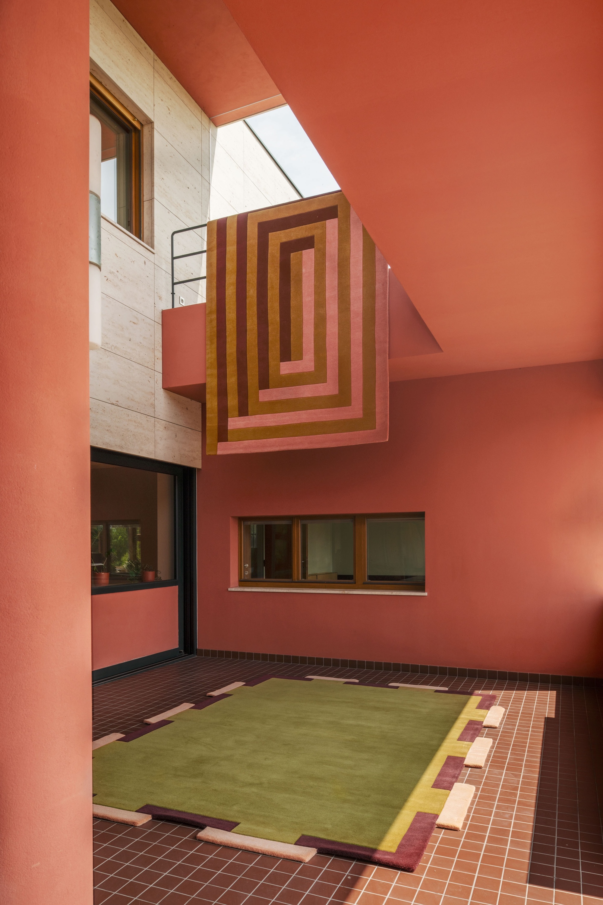 Image of a pink outdoor space with a large green rug on top of brown tile and a pink and orange rug hanging from an upper balcony.
