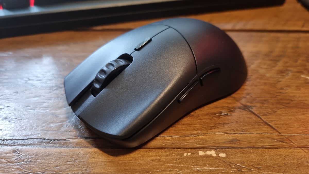 The Glorious Series 2 Pro Wireless gaming mouse on a wooden desk, with a red-lit keyboard just visible in the background of the shot.