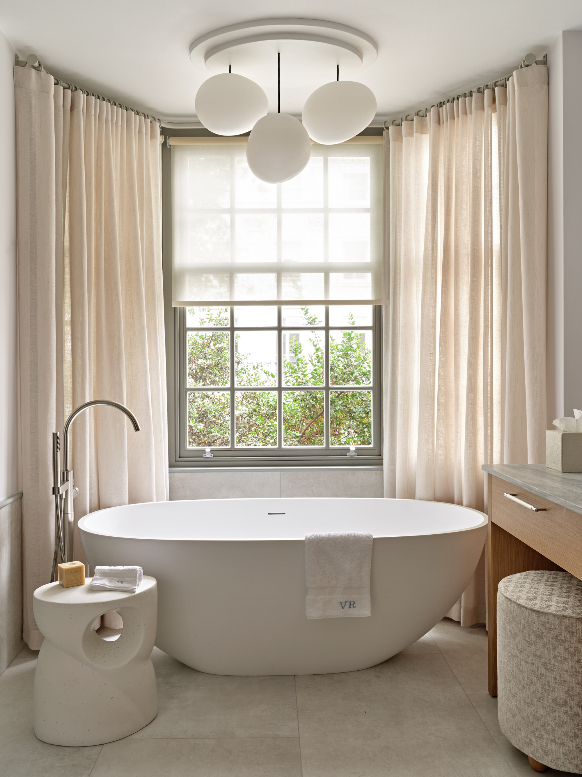 bathroom with cream curtains, sheer blind, freestanding bath, silver tapware, ottoman with soap, vanity with ottoman stool