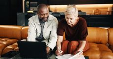 A mature couple sit on a sofa looking over their retirement accounts.