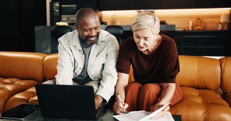A mature couple sit on a sofa looking over their retirement accounts.