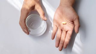 Woman's hand holding out vitamin D tablet next to other hand holding a glass of water