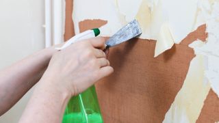 Wallpaper being sprayed with a water gun and scraped off using a putty knife