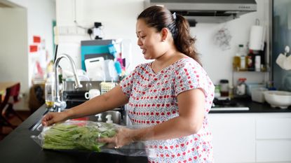 Woman in kitchen removing vegetables from a plastic wrapper