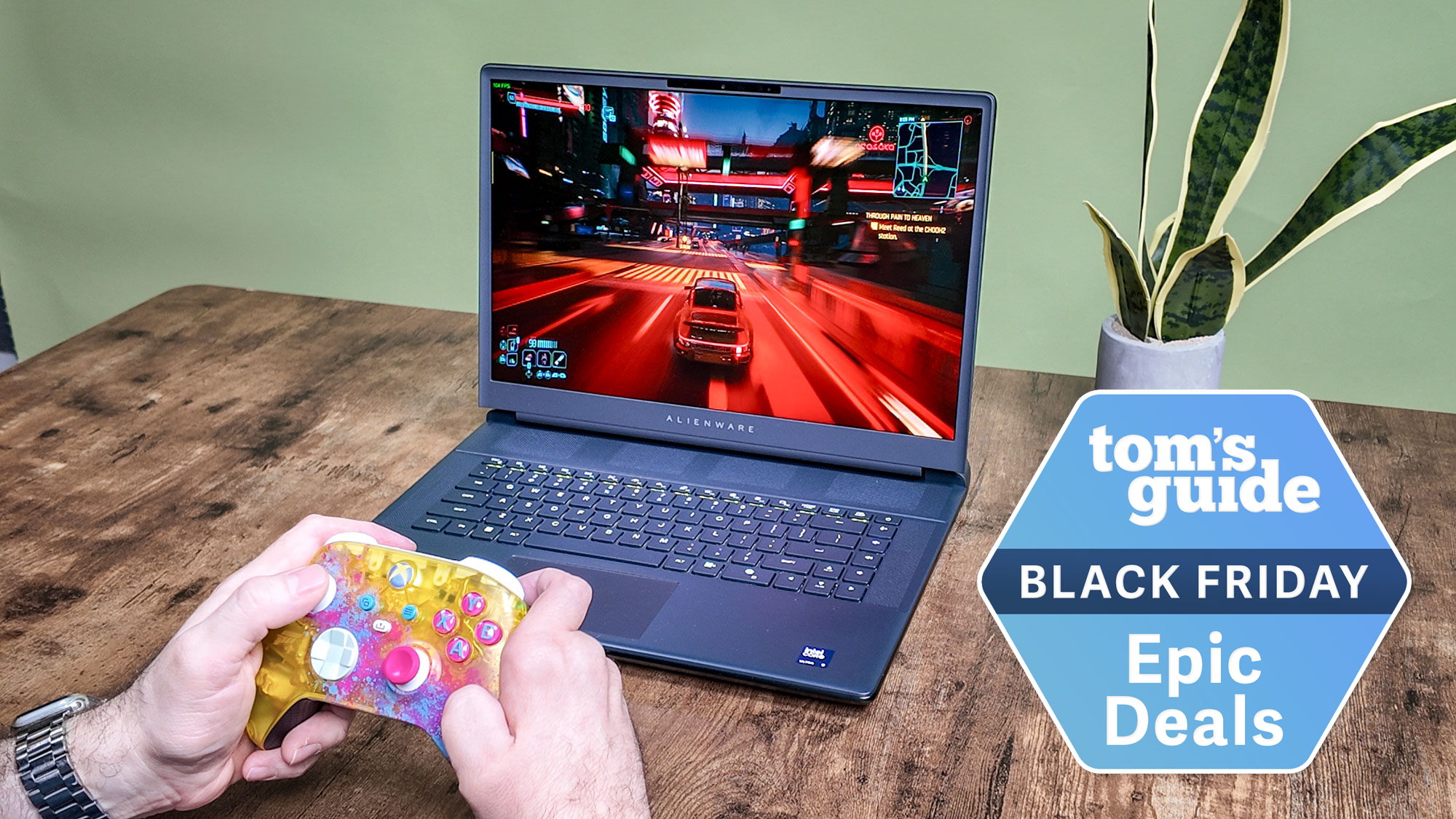 Alienware 16 Area-51 on table with hands using controller and Tom's Guide Black Friday Epic Deals badge