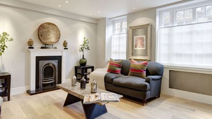 living room with white wall grey sofa with cushion white window and wooden flooring