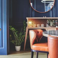 A dark blue dining room with orange and wood accents, with leather chairs and a marble table
