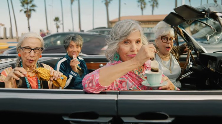 four older ladies in a car one of them has a cup of tea and a teabag in her hand