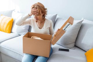 Wrong Item Concept. Sad unpset mature woman sitting on couch and unpacking cardboard box, received parcel with damaged staff, covering face in disappointment, feeling dissatisfied with bad purchase