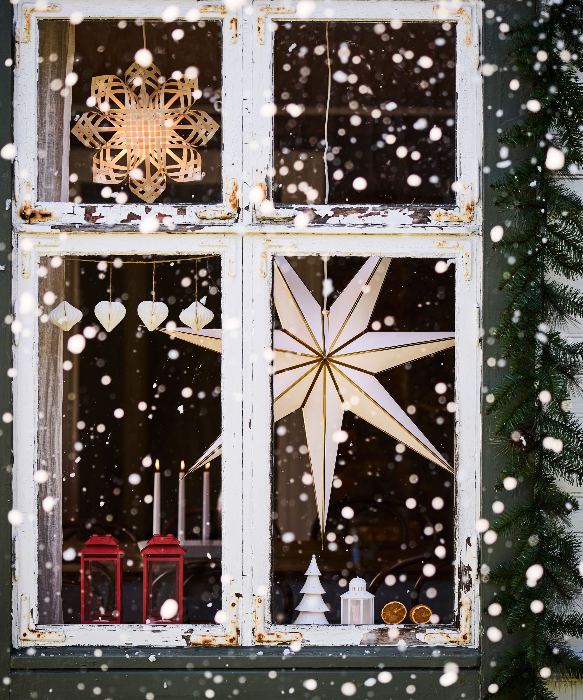 Paper stars hung at a white rustic window surrounded in evergreen and snow