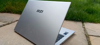A silver MSI Prestige 14 Evo B13M laptop sitting on a patio rock