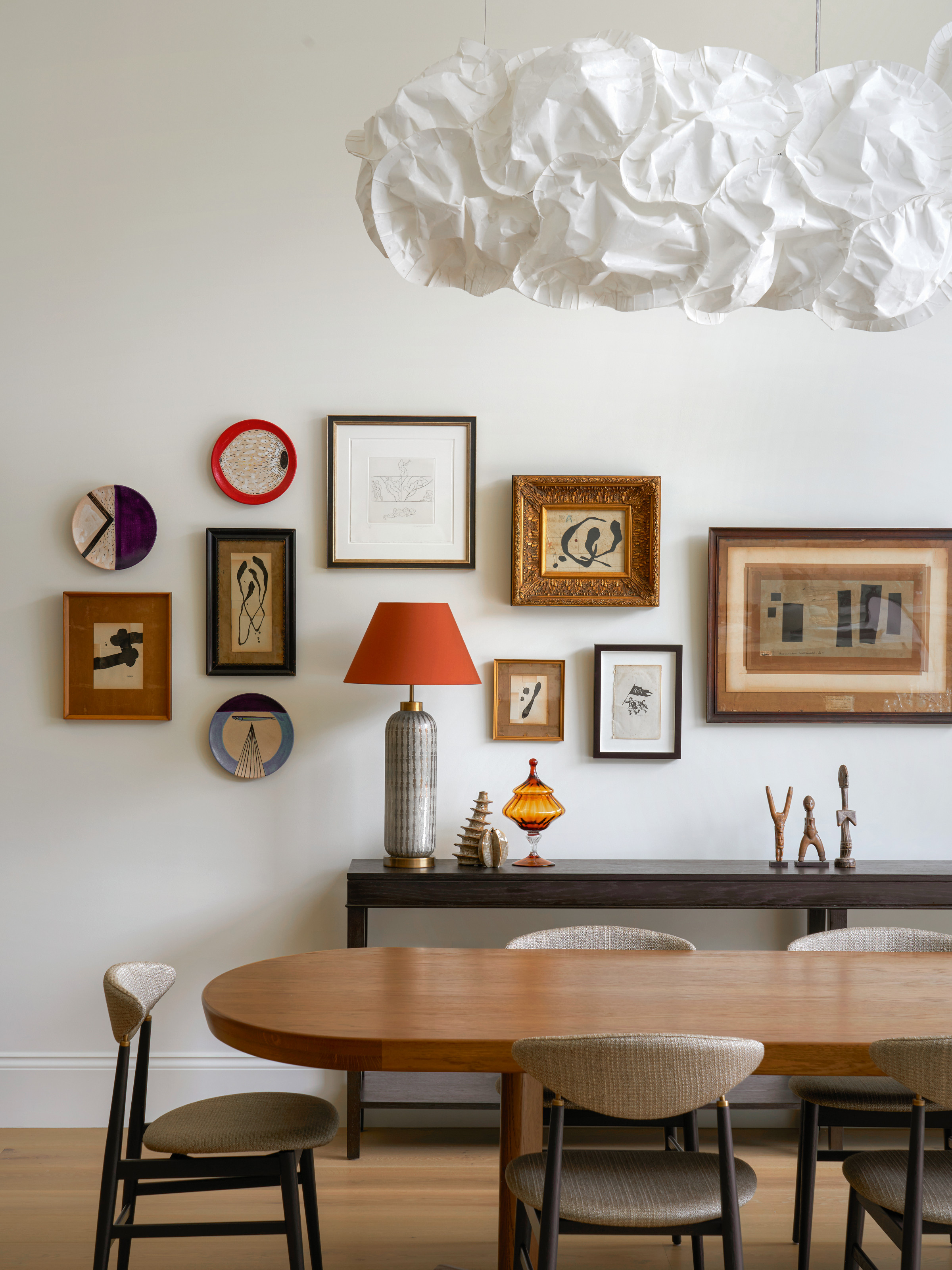Dining area with wooden table, beige chairs, gallery wall and cloud pendant light