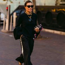 Woman wears black top and black track pants with printed heels. 