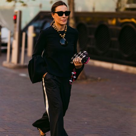 Woman wears black top and black track pants with printed heels. 