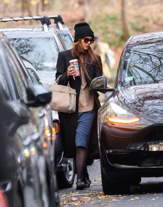 A photo of Katie Holmes layering semi-sheer black tights beneath blue bermuda shorts and a long black double-breasted coat.