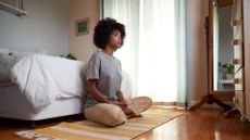 woman sitting on a rug on the floor in front of her bed cross legged in meditation 