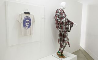 A white t-shirt with "God save the queen" hangs in a perspex box beside a mannequin wearing a tartan suit