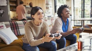 Laughing women friends playing video game on living room sofa