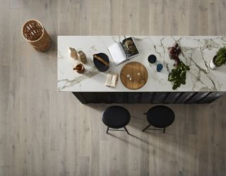 Aerial view of pale gray engineered wood kitchen flooring under a marble breakfast bar.