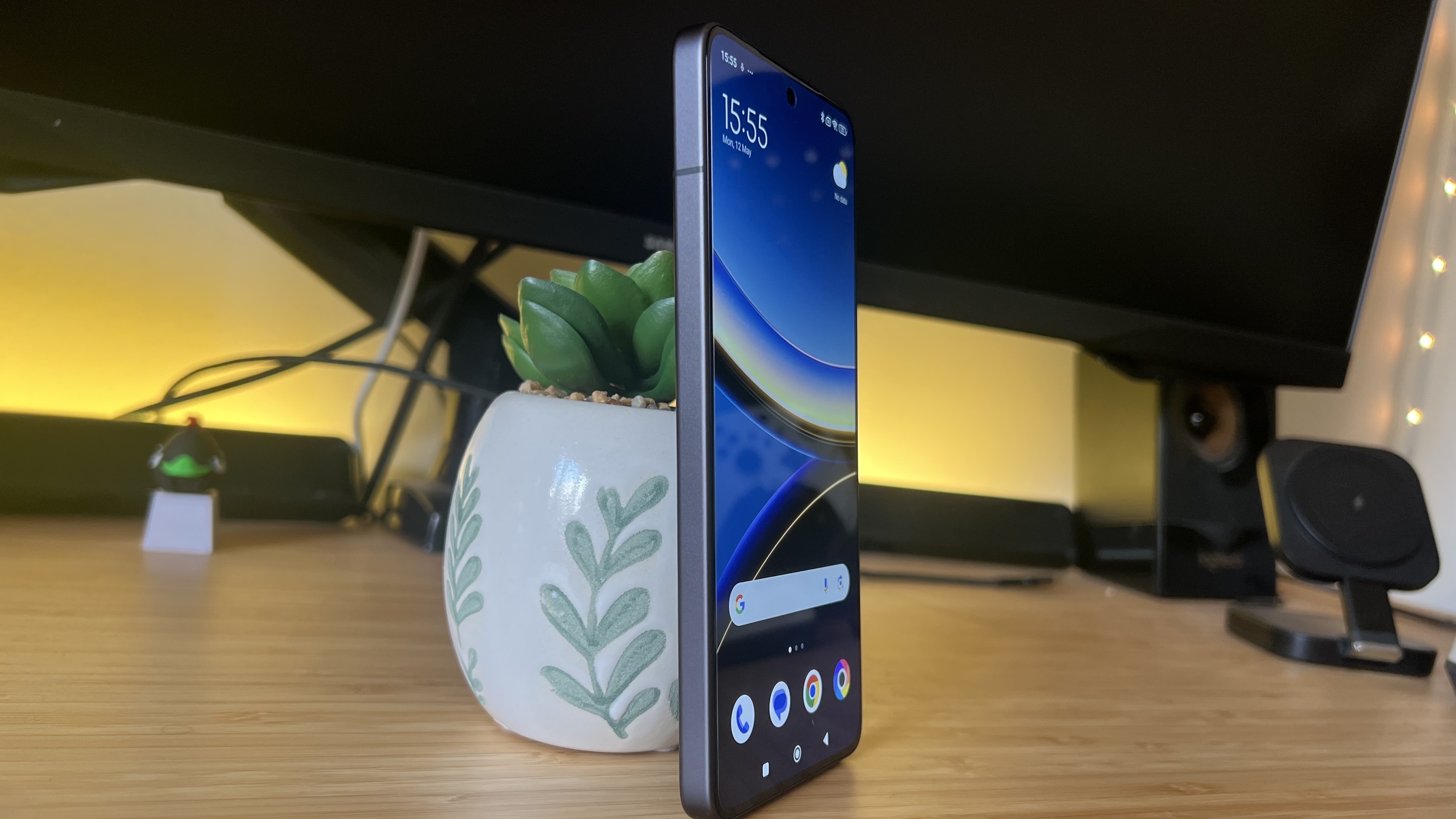 Side view of Poco F7 Pro phone leaning against a plant on a wooden desk