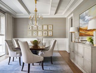 neutral dining room with wooden table, off white dining chairs, blue gray rug and chandelier