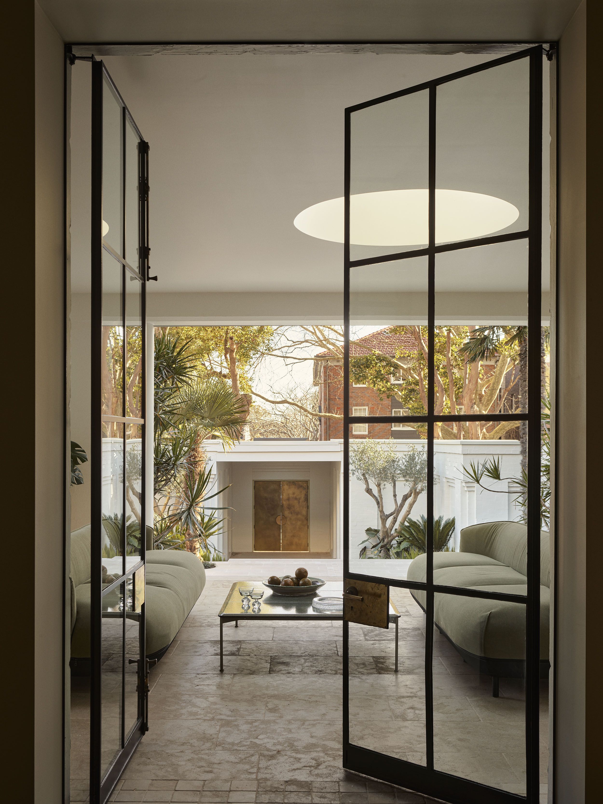 Steel-framed doors open from the living room onto the landscaped courtyard of Smac Studio's renovated Art Deco home, creating a seamless connection between indoor and outdoor living.