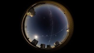 many bright dots can be seen in a starry night sky above a cluster of buildings in a desert