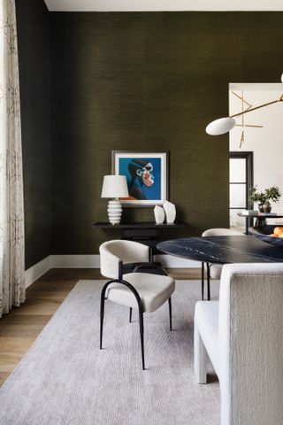 A dining room with white chairs, lighting and accessories, and a dark green wall