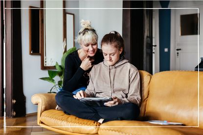 Mother helping teenage daughter on laptop while sat on the sofa