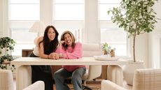 Joanna gaines and Hoda in office space with cream wood desk, potted tree and plaid armchairs