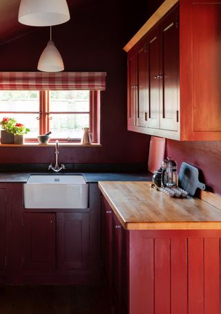 A kitchen with a butler sink and wooden cabinets painted red