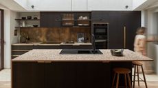 modern kitchen with black cabinets, brass backsplash, terrazzo countertop, and gold hardware