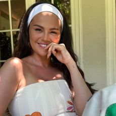 A photo of selena gomez outside on a porch wearing a white headband matching a dress by free people