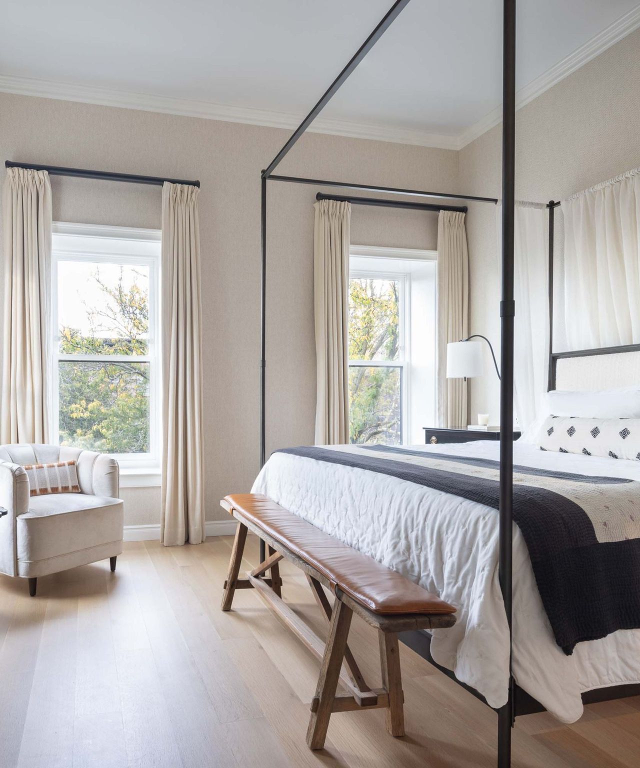 A brownstone bedroom with a four-poster bed, bench, and hardwood floors
