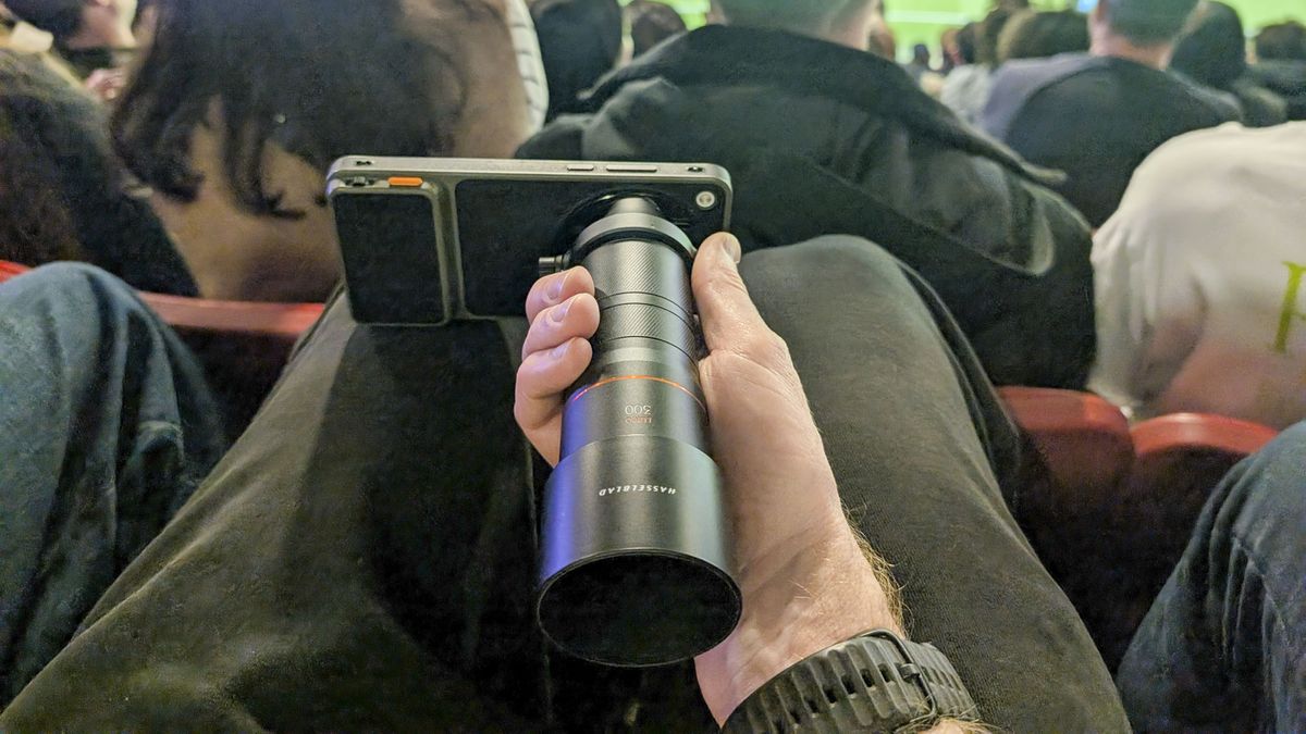 Oppo Find X9 Ultra with teleconverter lens attached, in the hand of user in the crowd at a soccer match