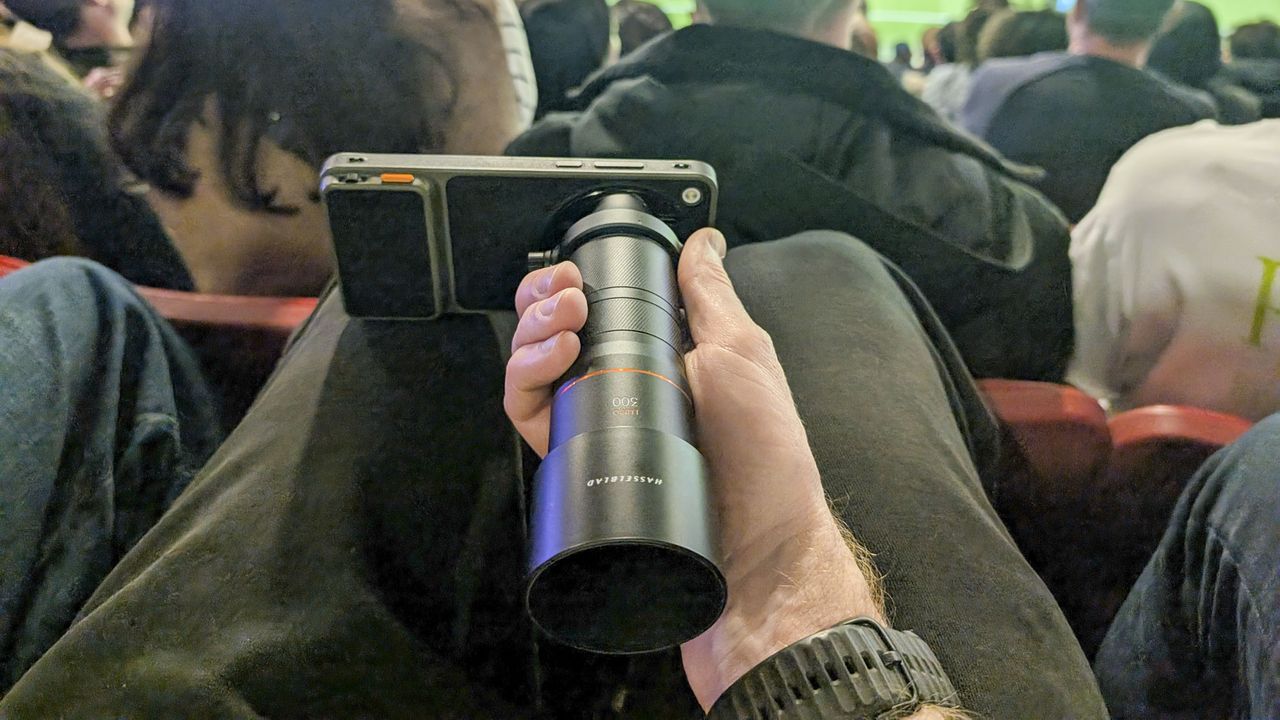 Oppo Find X9 Ultra with teleconverter lens attached, in the hand of user in the crowd at a soccer match
