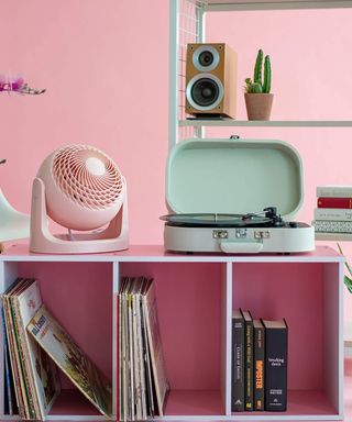 A pink fan on a shelving unit next to a record player.