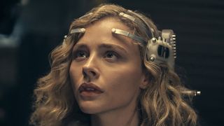 Flynne Fisher i sci-fi-serien The Peripheral sitter med sitt VR-headset på huvudet och tittar upp på något.