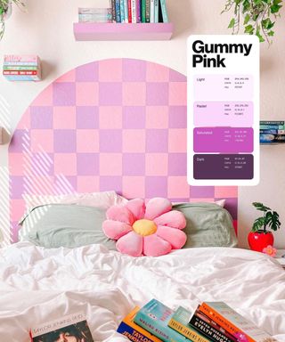 A bed with white bedding, sage green accent pillows, a flower-shaped throw cushion, and a lilac and pink painted checker headboard, surrounded by floating bookshelves and with Pinterest's Gummy Pink swatch overlaid
