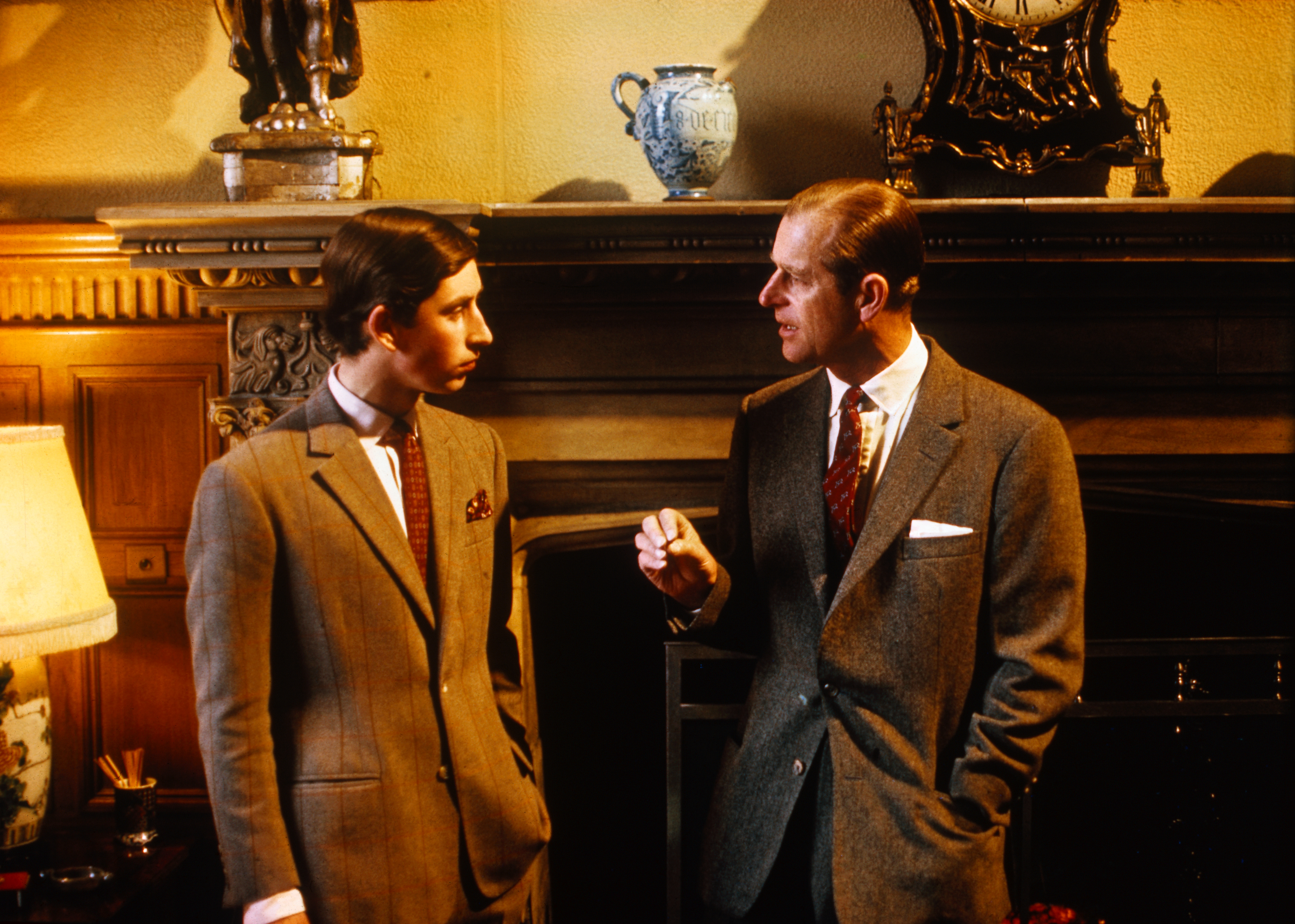 Prince Philip talking to Prince Charles in front of a fireplace