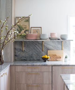 A corner of a small kitchen with wood cabinets and draws, gray marble countertops and backsplash, and traditional style decor