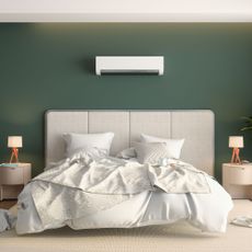 air conditioning unit on a dark green wall above a large bed with light headboard and bedding, and two side tables with small lamps