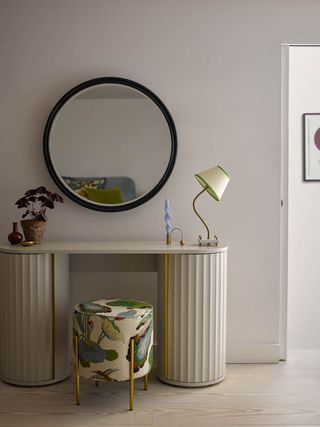 An entryway console table with a fluted base, a round mirror, and a wavy table lamp